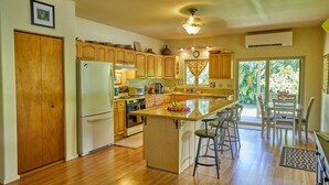 A spacious kitchen with wooden cabinets, a central island with bar stools, a refrigerator, and a stove. - Hawaiian plantation-style home, perfect for families.  (Hauula)