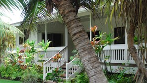 A white house with a porch, surrounded by lush greenery and palm trees. - Hawaiian plantation-style home, perfect for families.  (Hauula)
