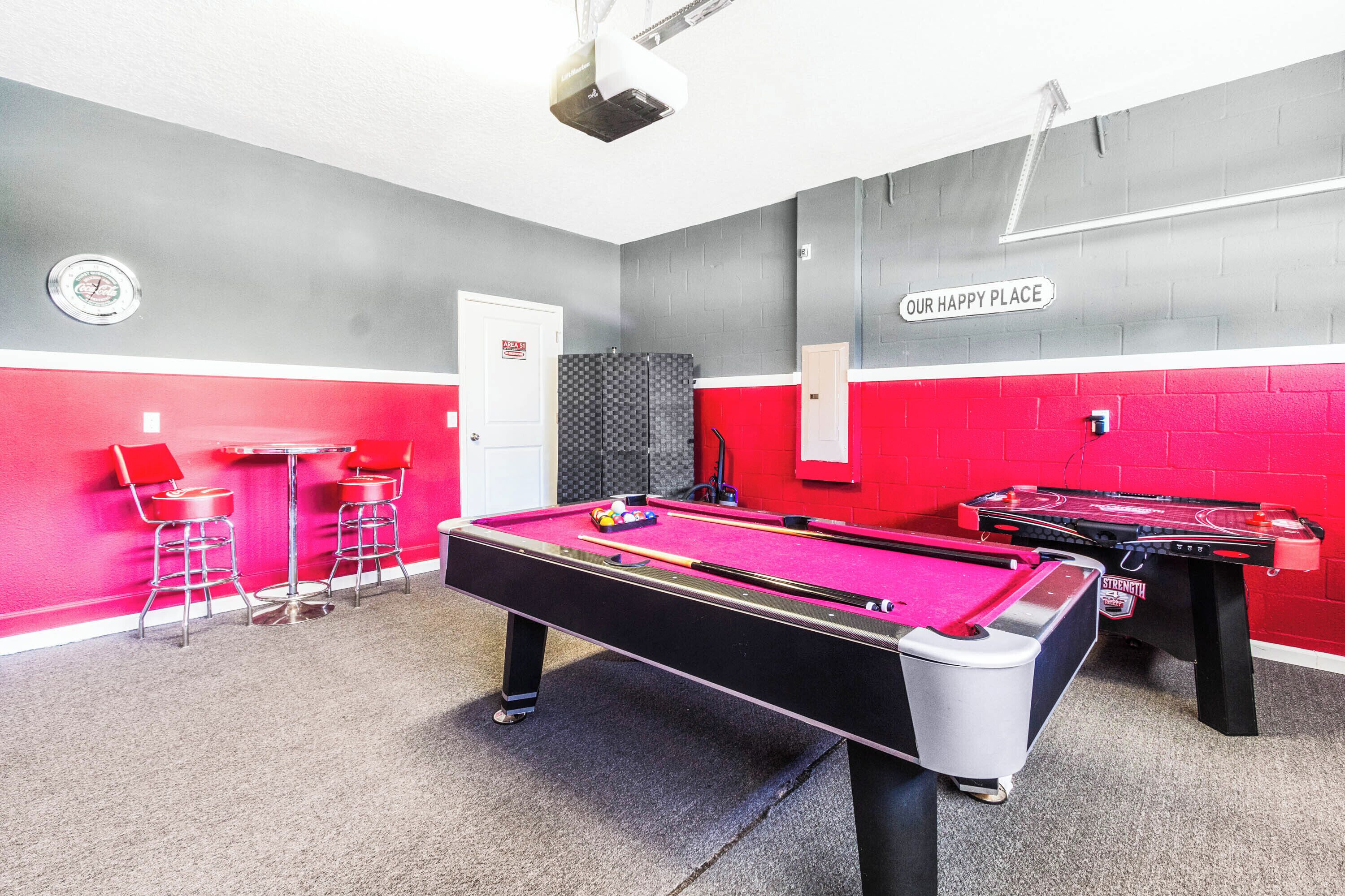 A pool table with red and black stools, a dartboard, and a sign reading "OUR HAPPY PLACE".