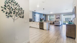Una cocina moderna con una isla central, armarios blancos y lavavajillas. Hay un comedor con sofá y mesa de centro.
