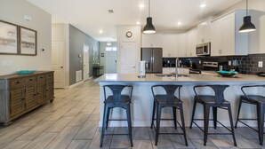 Una cocina moderna con una isla grande, taburetes de bar y electrodomésticos de acero inoxidable.