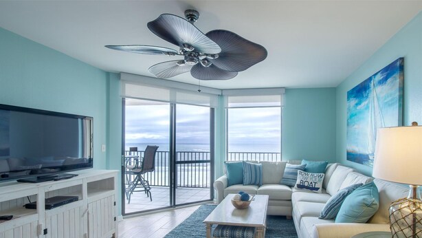 Ein Wohnzimmer mit Fernseher, Deckenventilator, Sofa und Balkon mit Meerblick.