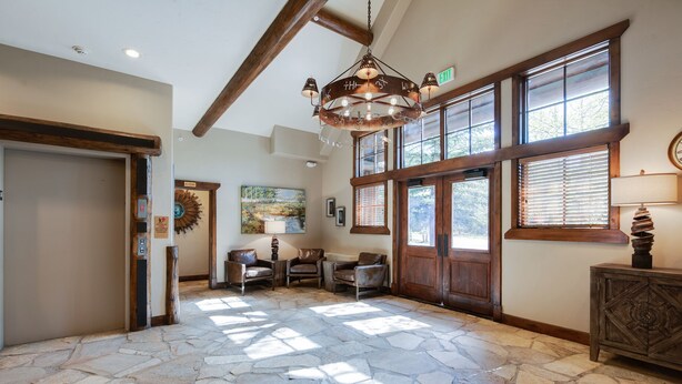 A stone-floored lobby with a chandelier, wooden beams, and large windows. - Corral at Breckenridge Raven Condo: Soaking Tub, Views (Breckenridge)