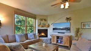 A cozy living room with a fireplace, a television, and a stone fireplace surround. - Corral at Breckenridge Raven Condo: Soaking Tub, Views (Breckenridge)