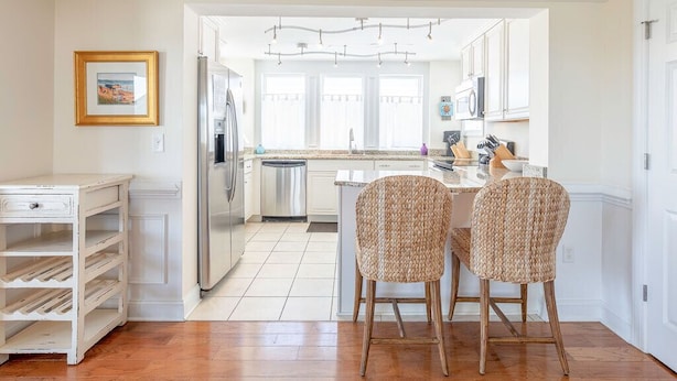 Una cocina moderna con muebles blancos, un refrigerador de acero inoxidable y un comedor con dos sillas de mimbre.