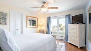 Un dormitorio con cama, ventilador de techo, cómoda, televisor y ventana con cortinas.