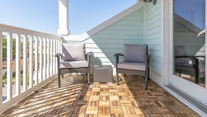 Un patio techado con dos sillas de mimbre y un pequeño reposapiés, piso de madera y vistas del entorno.