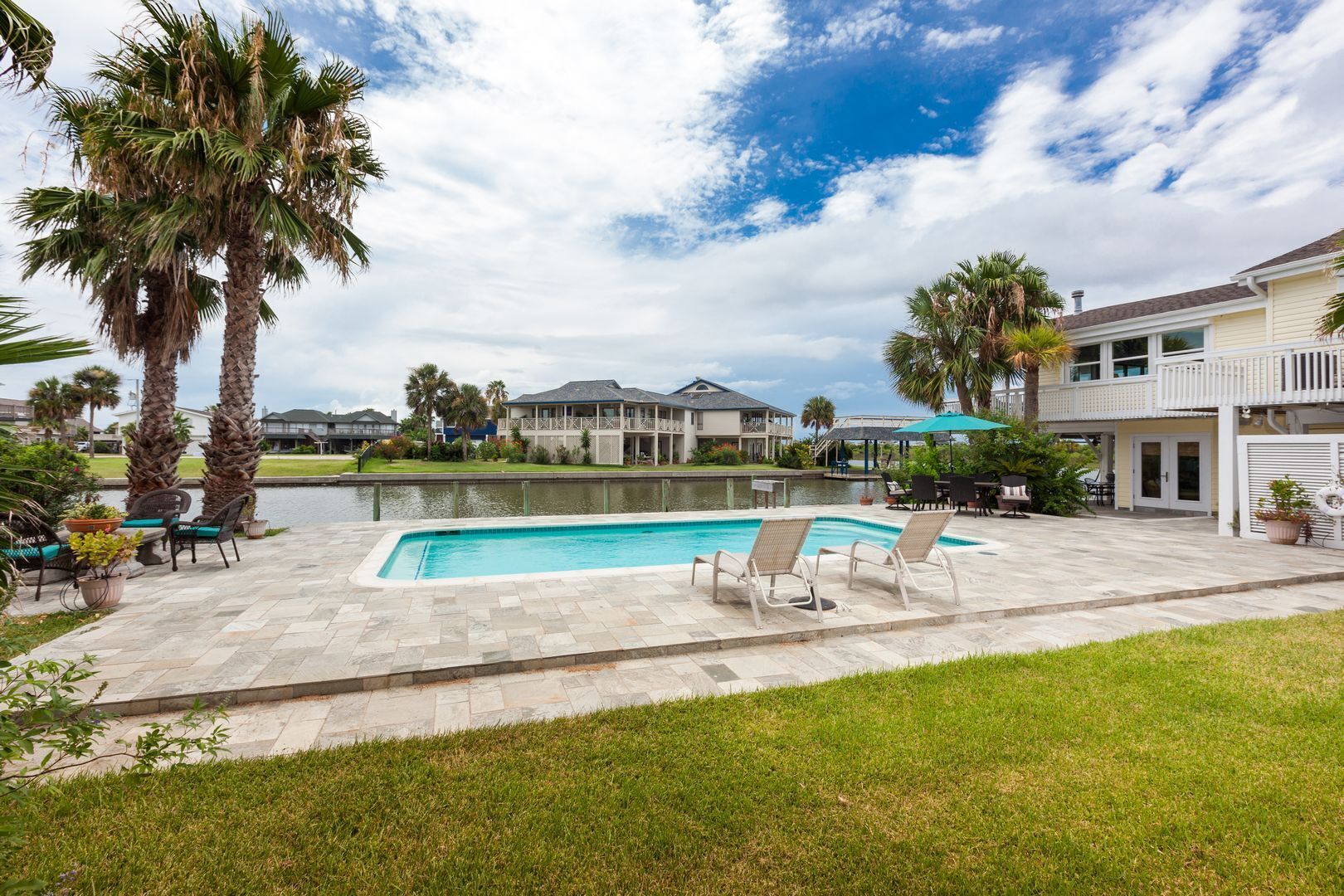 Une piscine entourée de chaises longues et de palmiers, ainsi qu’une maison dotée d’un balcon.