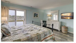 A bedroom with a bed, a desk, a dresser, a chair, a window with curtains, and a painting on the wall. - 1607 Port Villas - Gorgeous views of Braddock Cove (Hilton Head Island)