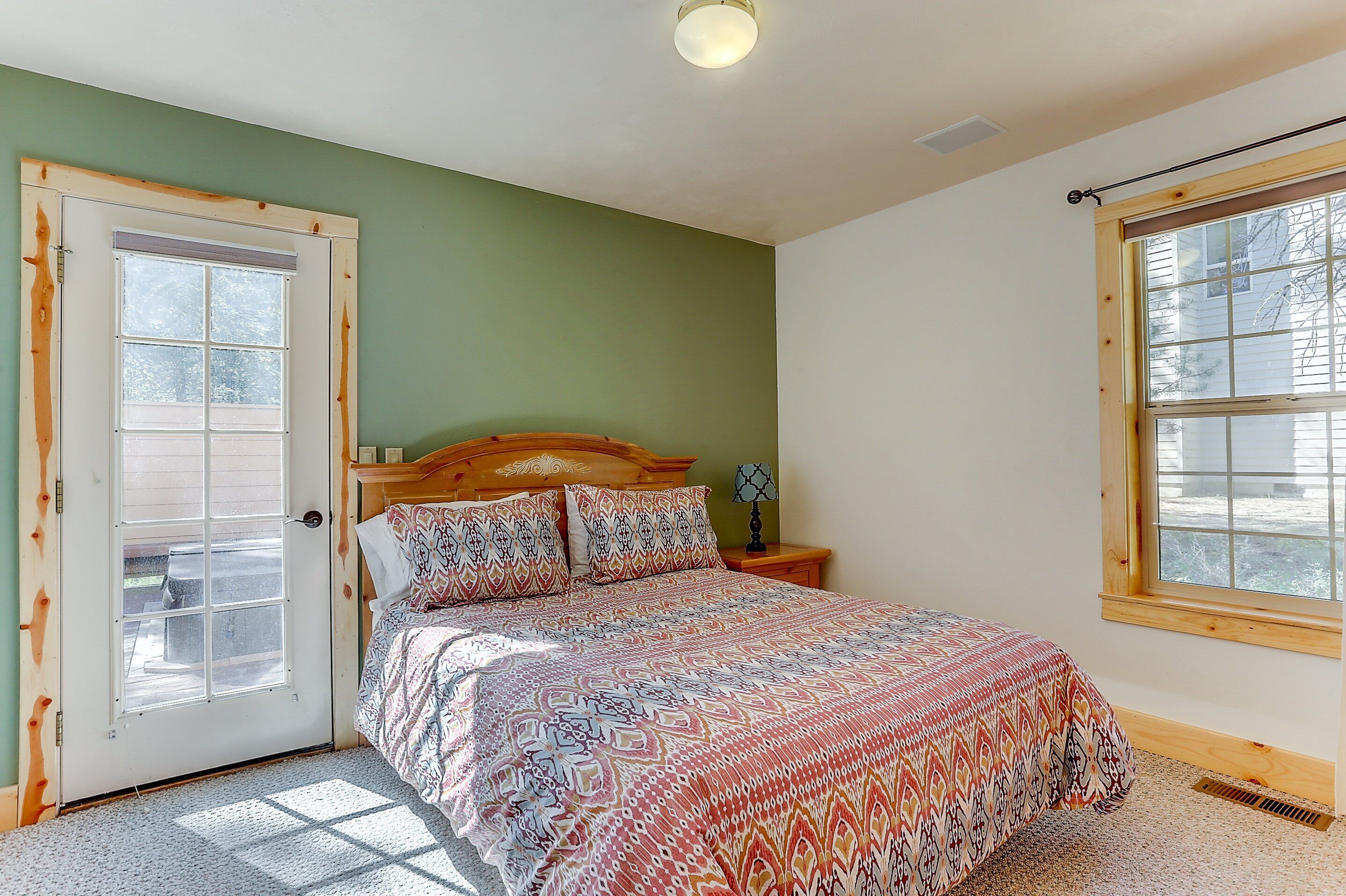 A bedroom with a bed, a nightstand, a lamp, a window, and a door.