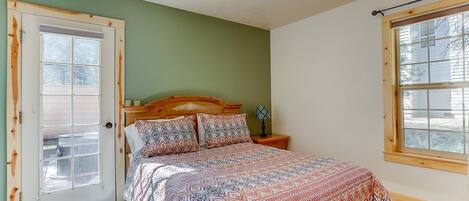 A bedroom with a bed, a nightstand, a lamp, a window, and a door.