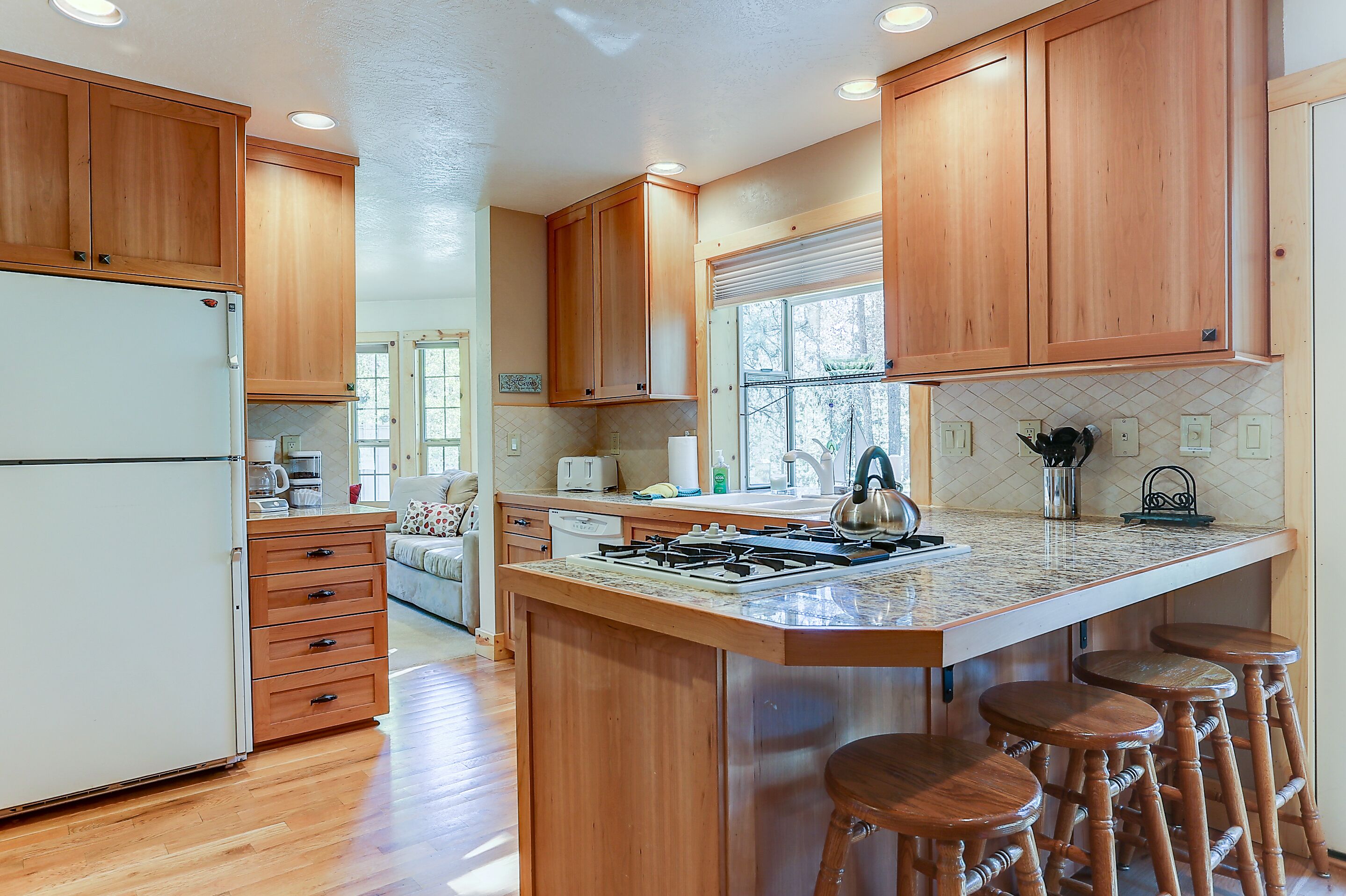 A kitchen with wooden cabinets, a refrigerator, a stove, and bar stools.