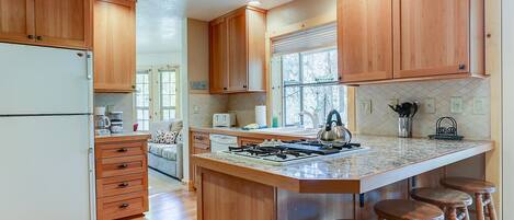 A kitchen with wooden cabinets, a refrigerator, a stove, and bar stools.
