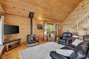 A cozy cabin interior with a fireplace, leather sofa, and wooden walls. - Secluded Log Cabin on Wildlife Preserve | Mt. Mitchell Views, Game Loft & 3 Decks (Old Fort)