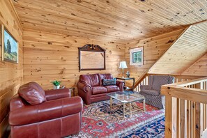 A cozy cabin interior with a wooden ceiling, a leather sofa, a patterned rug, and a staircase. - Secluded Log Cabin on Wildlife Preserve | Mt. Mitchell Views, Game Loft & 3 Decks (Old Fort)
