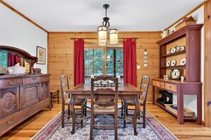 Ein Holzinterieur mit einem Esstisch, Stühlen, einer Chandelieber und einem Schrank mit dekorativen Tellern.