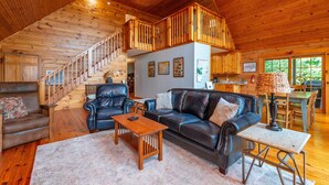 A spacious living room with a wooden staircase, leather furniture, and a dining area. - Secluded Log Cabin on Wildlife Preserve | Mt. Mitchell Views, Game Loft & 3 Decks (Old Fort)