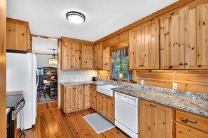 A kitchen with wooden cabinets, a granite countertop, a sink, and a dishwasher. - Secluded Log Cabin on Wildlife Preserve | Mt. Mitchell Views, Game Loft & 3 Decks (Old Fort)