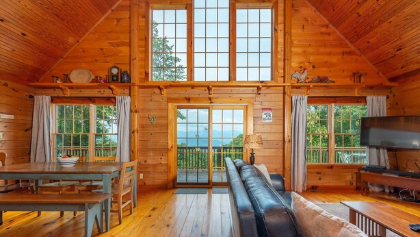 A log cabin interior with a dining area, a sofa, and a television. - Secluded Log Cabin on Wildlife Preserve | Mt. Mitchell Views, Game Loft & 3 Decks (Old Fort)