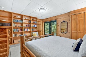 Ein Schlafzimmer mit einem großen Bett, Holzregalen, einem Spiegel und Blick ins Freie.