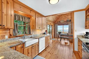 Interior de una cabaña de madera con cocina, comedor y un amplio ventanal.