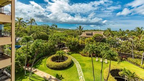 A lush garden with palm trees, a circular lawn, and a building with a tiled roof.