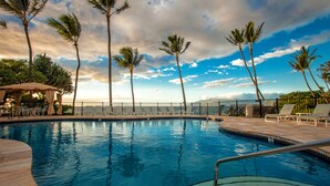 A swimming pool with lounge chairs and palm trees, surrounded by a fence.