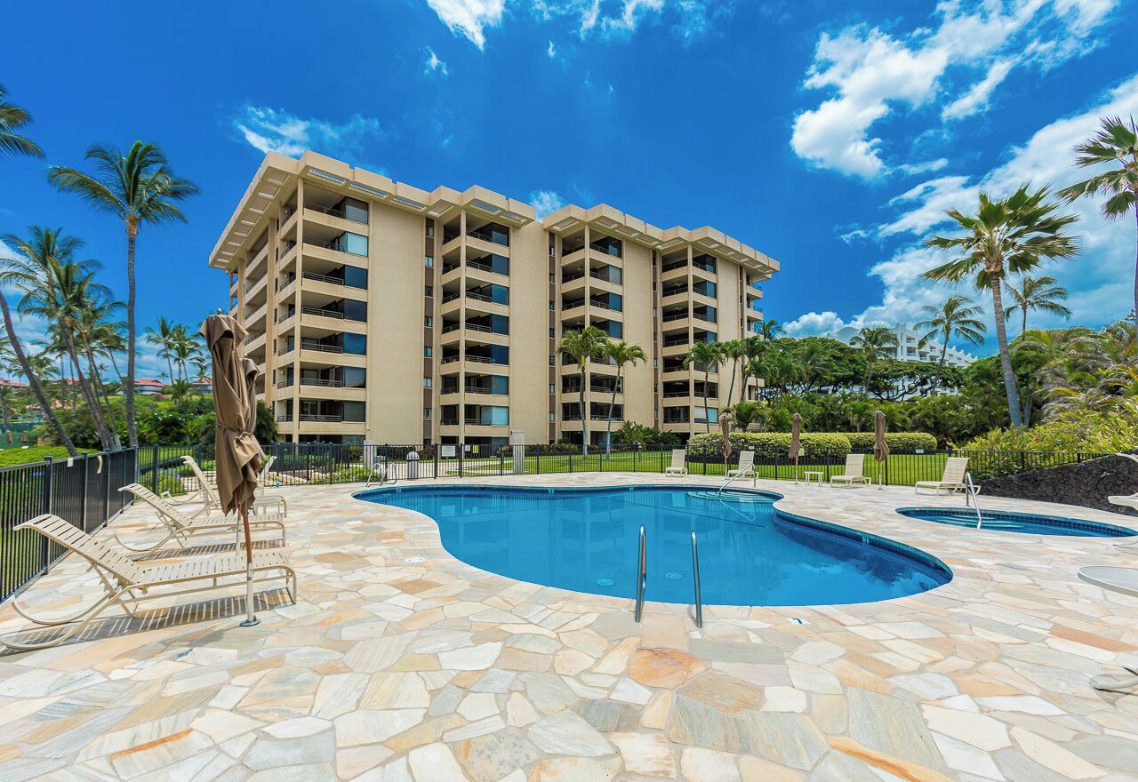 A hotel with a pool area, multiple lounge chairs, and palm trees.