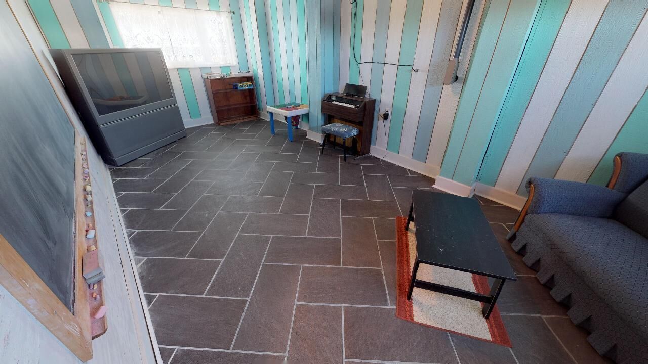 A room with a tiled floor, a sofa, a small table, a piano, and a television.