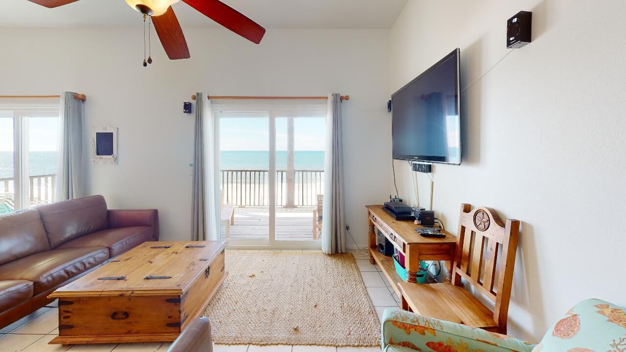 Una sala de estar con sofá, mesa de centro, televisor y vista a la playa.