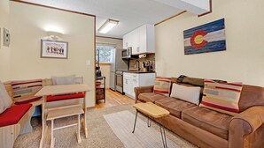 Una sala de estar acogedora con un sofá marrón, una mesa de madera y una cocina al fondo.