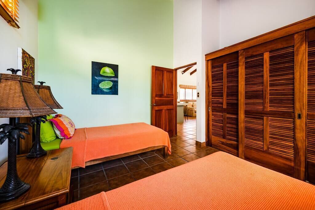 Une chambre avec deux lits, une armoire en bois, une table avec une lampe et un tableau au mur.