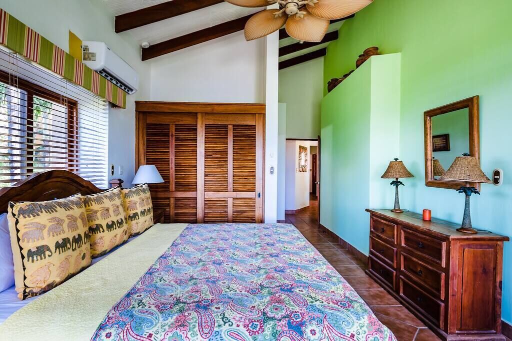 A bedroom with a bed, a wooden wardrobe, a dresser, and a ceiling fan.