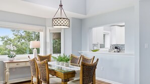 A dining area with a glass-top table, wicker chairs, a hanging light fixture, and a view of the outdoors.
