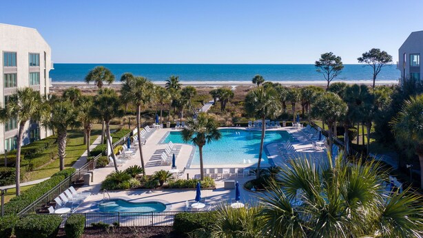 A resort with a large pool, sun loungers, and a view of the beach and ocean.