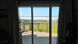 Una habitación con puerta corrediza de vidrio que da a una terraza de madera con vistas a un césped.