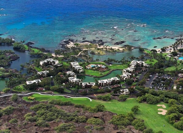 Vista aérea de um resort costeiro com vários edifícios, um campo de golfe e uma marina.