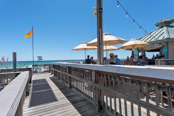 Een houten terras met parasols en een vlag, met uitzicht op een strand.
