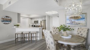 A modern kitchen with white cabinets, a central island, and a dining area with a round table and patterned chairs. - St. Lucia 904 ~  9th Floor ~ Amazing Views! (Destin)