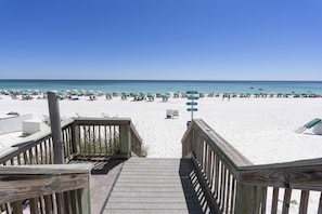 Een houten trap die uitkomt op een strand met wit zand en turquoise water.