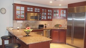 A kitchen with wooden cabinets, a stainless steel refrigerator, a microwave, a sink, and a fruit bowl on the counter.