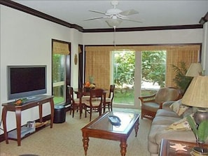 Relax in this stylish living room with a sofa, dining area, and large windows offering a view of the surrounding greenery.