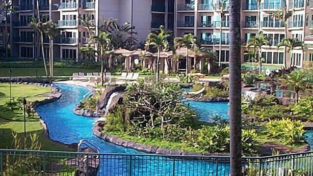 A resort with a central swimming pool, surrounded by lush greenery and palm trees.