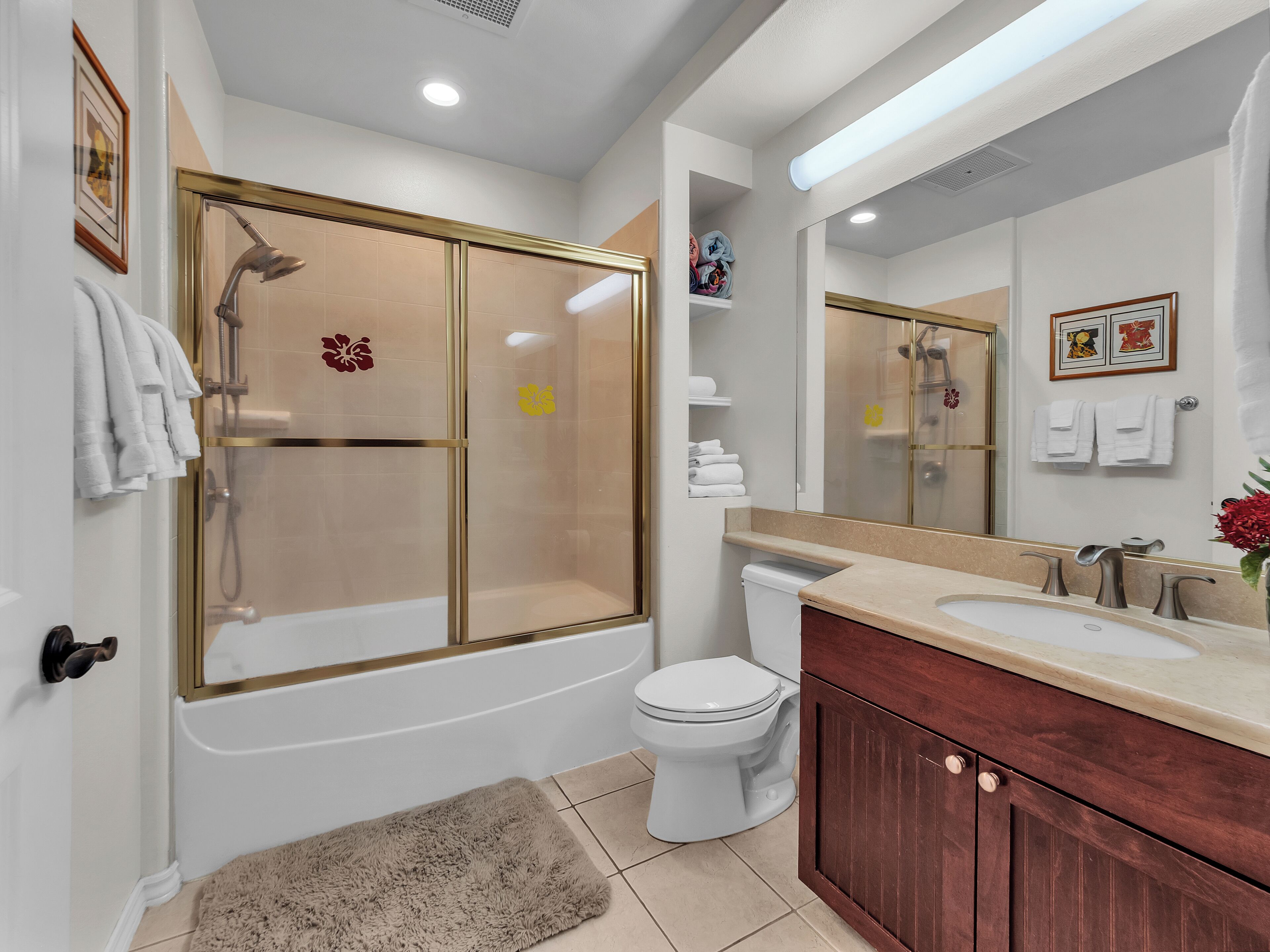 A modern bathroom with a glass-enclosed shower, a white toilet, a beige bath tub, and a wooden vanity with a mirror.