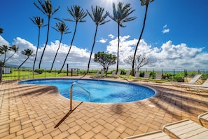 A swimming pool with a brick deck, surrounded by palm trees and lounge chairs.