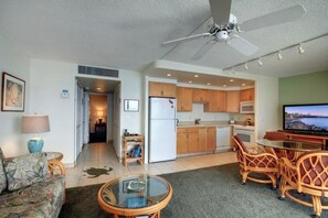 A living room with a sofa, a glass coffee table, a television, and a dining area with wicker chairs.