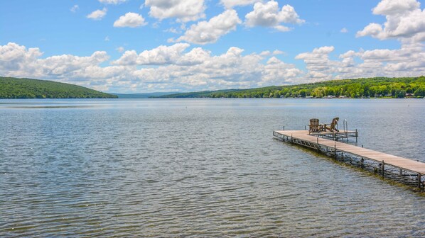 A wooden pier extending into calm waters with a clear sky and distant green hills. - Serenity Cove - Charming, Cozy Keuka Lake Cottage! (Branchport)