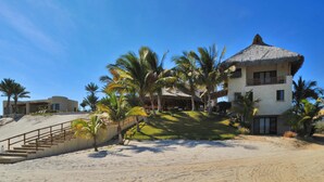 A beachfront property with a thatched-roof building, palm trees, and a staircase leading to a sandy area. - Full Staff Beachfront Estate w/ 2 Villas, Pool, Tennis Court & Cook Cabo (La Paz)