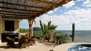 An outdoor patio with wicker furniture, a pool, and cacti. - Full Staff Beachfront Estate w/ 2 Villas, Pool, Tennis Court & Cook Cabo (La Paz)