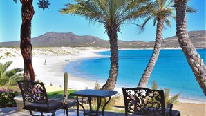 A beachside patio with two chairs and a table, overlooking a sandy beach and clear blue waters. - Full Staff Beachfront Estate w/ 2 Villas, Pool, Tennis Court & Cook Cabo (La Paz)